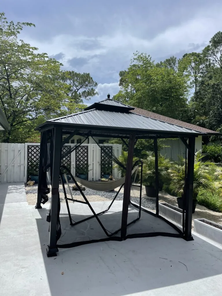 Dark roofed gazebo with a hanging swing on a concrete backyard patio