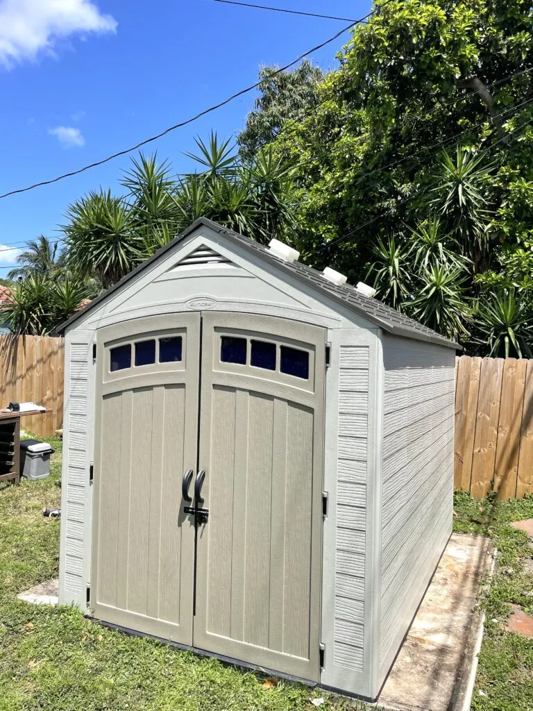 Beige resin shed with upper door windows and a dark pitched roof in a fenced yard