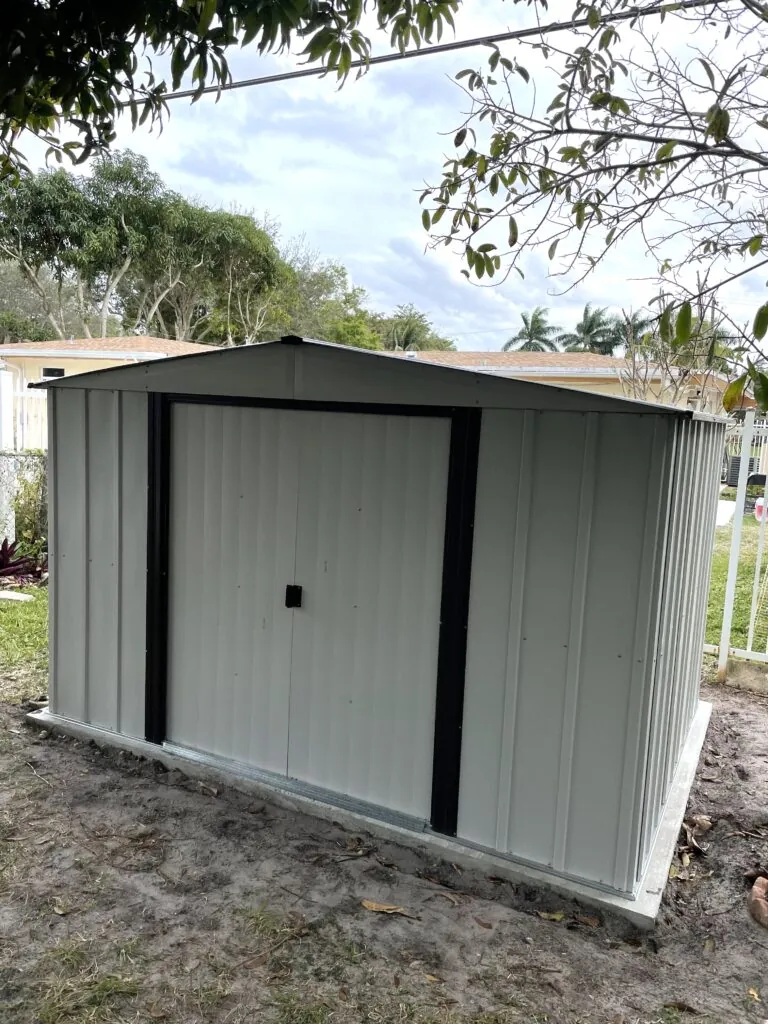 Gray metal garden shed on a concrete base beneath a shady tree