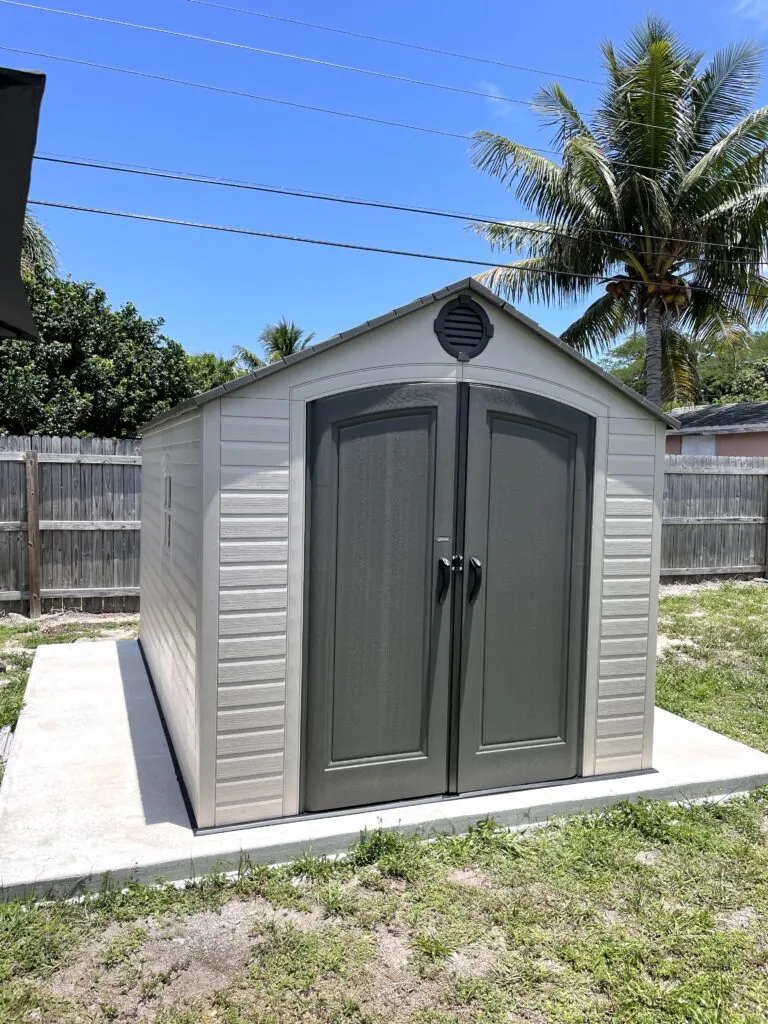 Gray resin shed with a gable vent and double doors on a concrete slab