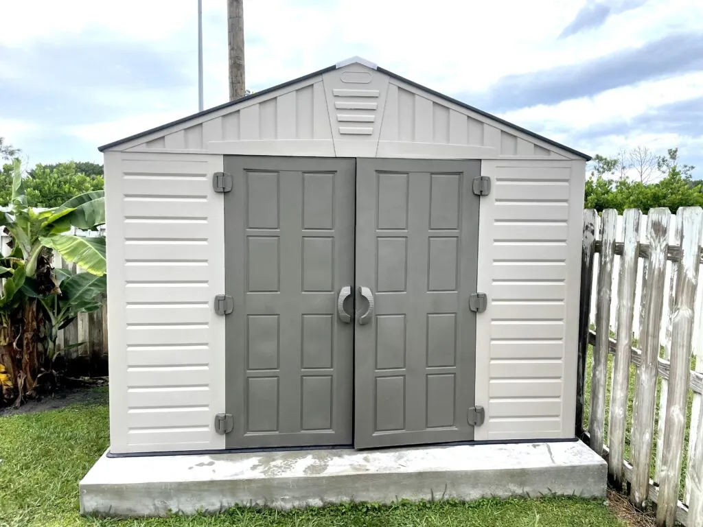 A complete light gray resin shed with double doors on a level concrete slab, assembled by David in South Florida